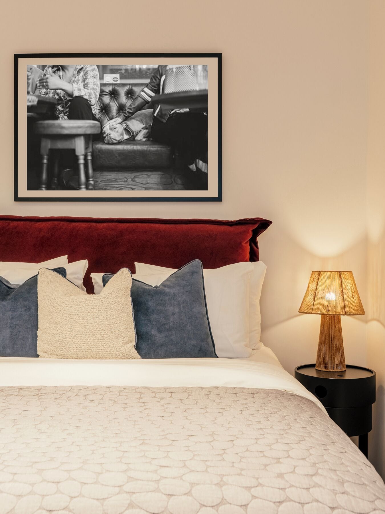 Una cama con cubrecamas estampado, cabecera roja y una fotografía blanco y negro enmarcada encima.