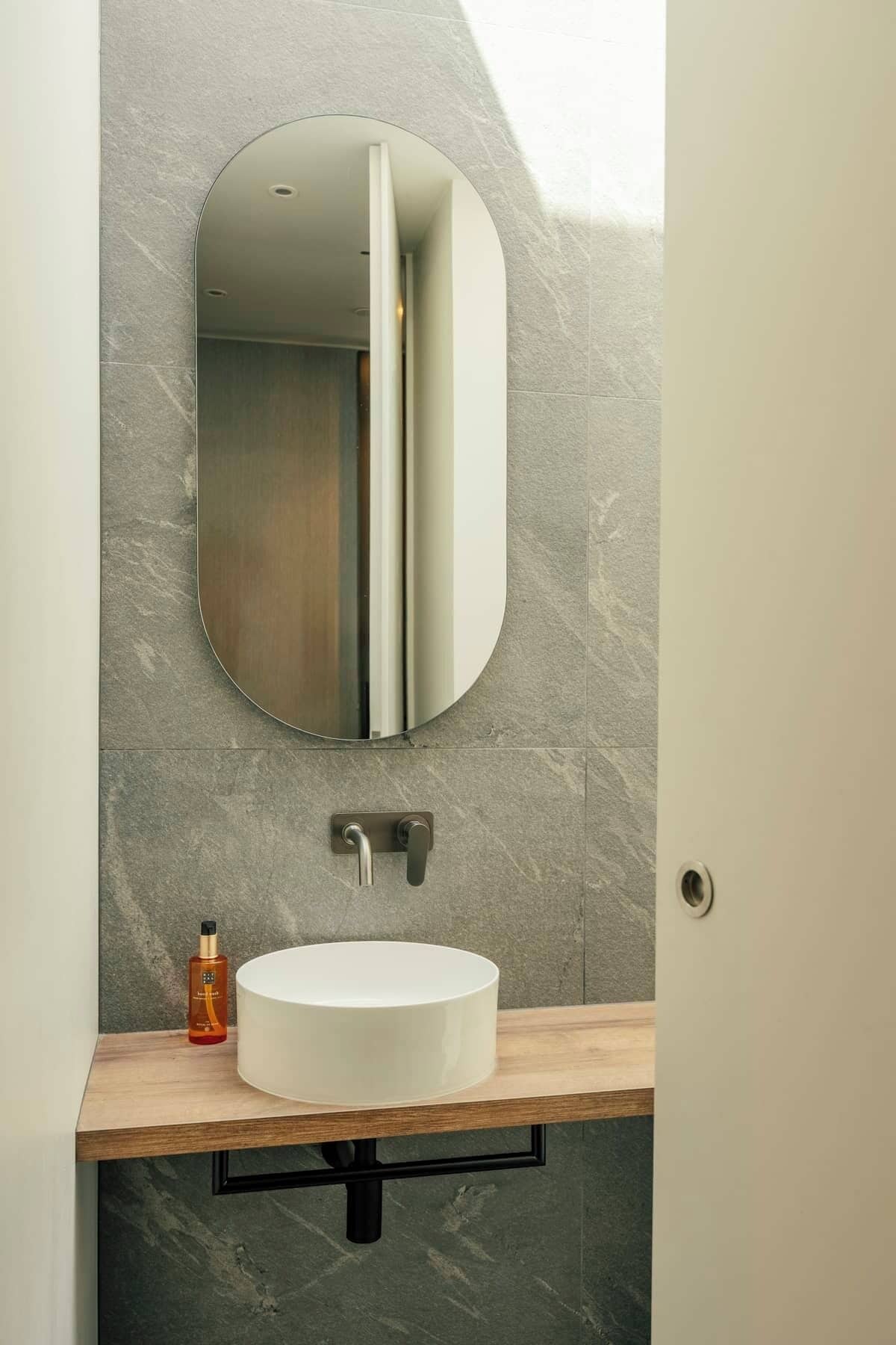 Un baño con un lavamanos blanco y redondo, un espejo y una botella de jabón para manos.
