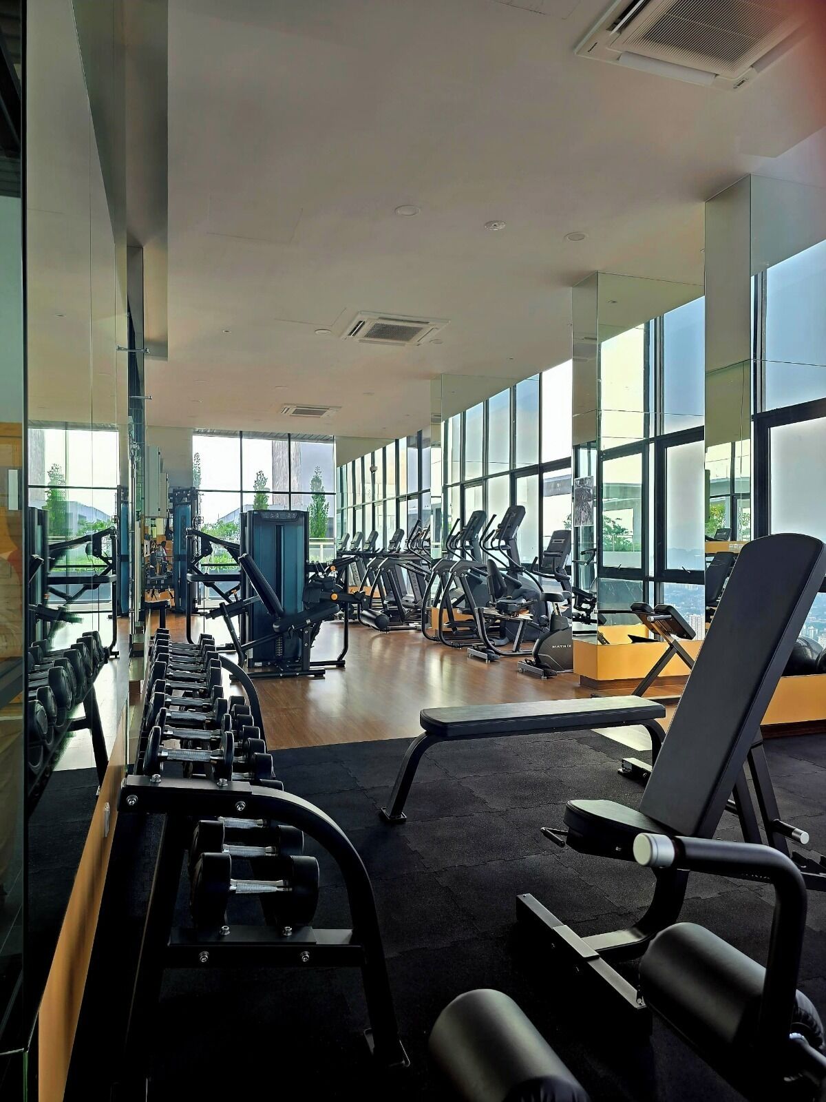 Uma academia com diversos equipamentos de exercícios, amplas janelas e um balcão de recepção.