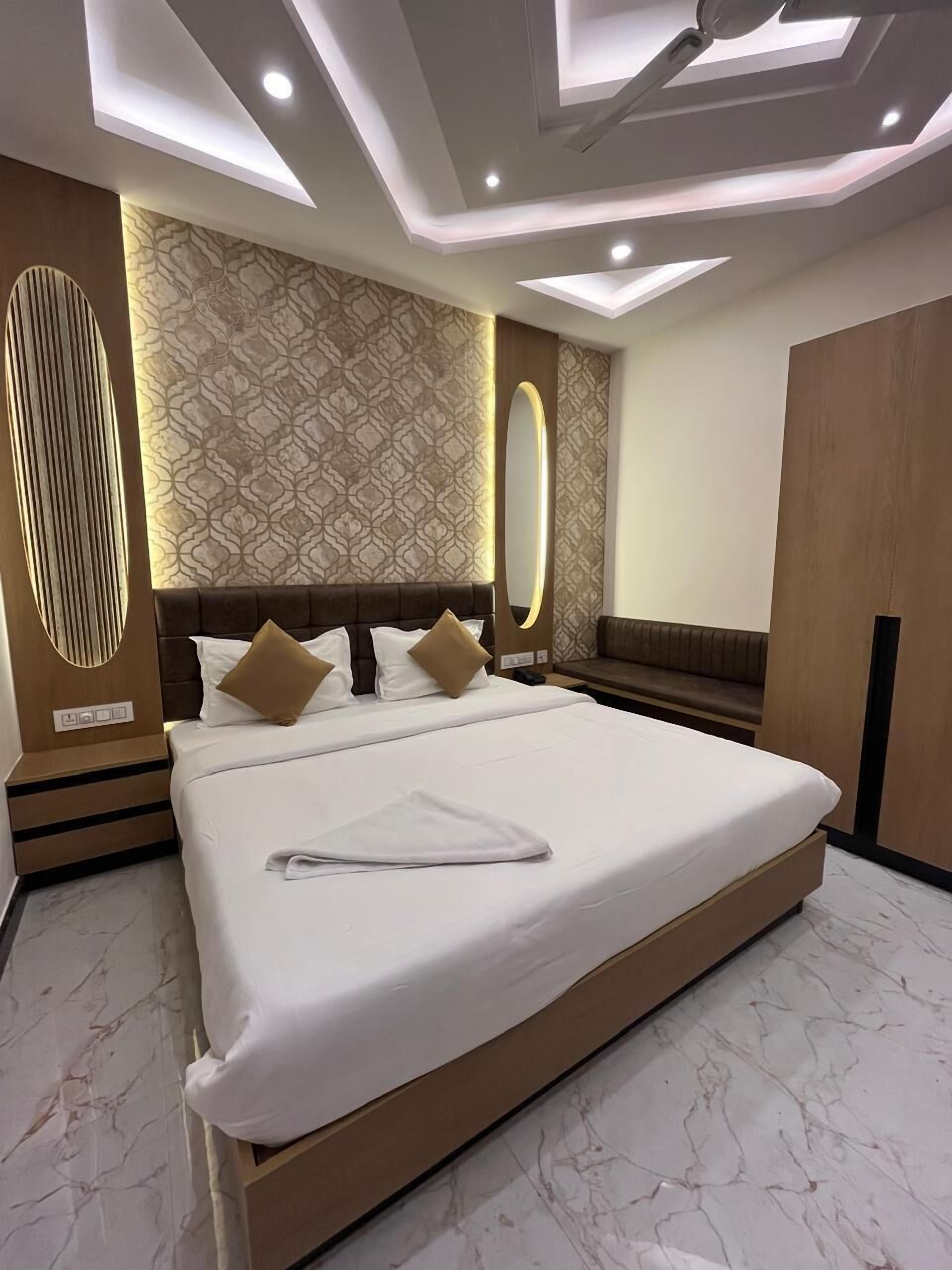 Una habitación de hotel moderna con una cama grande, cabecera de madera, papel tapiz estampado e iluminación empotrada en el techo.