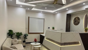 A modern reception area with a white reception desk, a sofa, and two small tables. - Uptown Inn (Bengaluru)