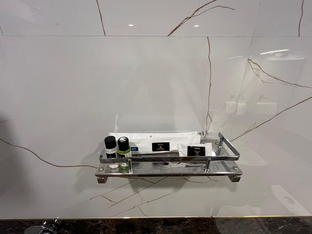 A bathroom with a white marble wall, a metal shelf with toiletries, and a visible crack in the wall.
