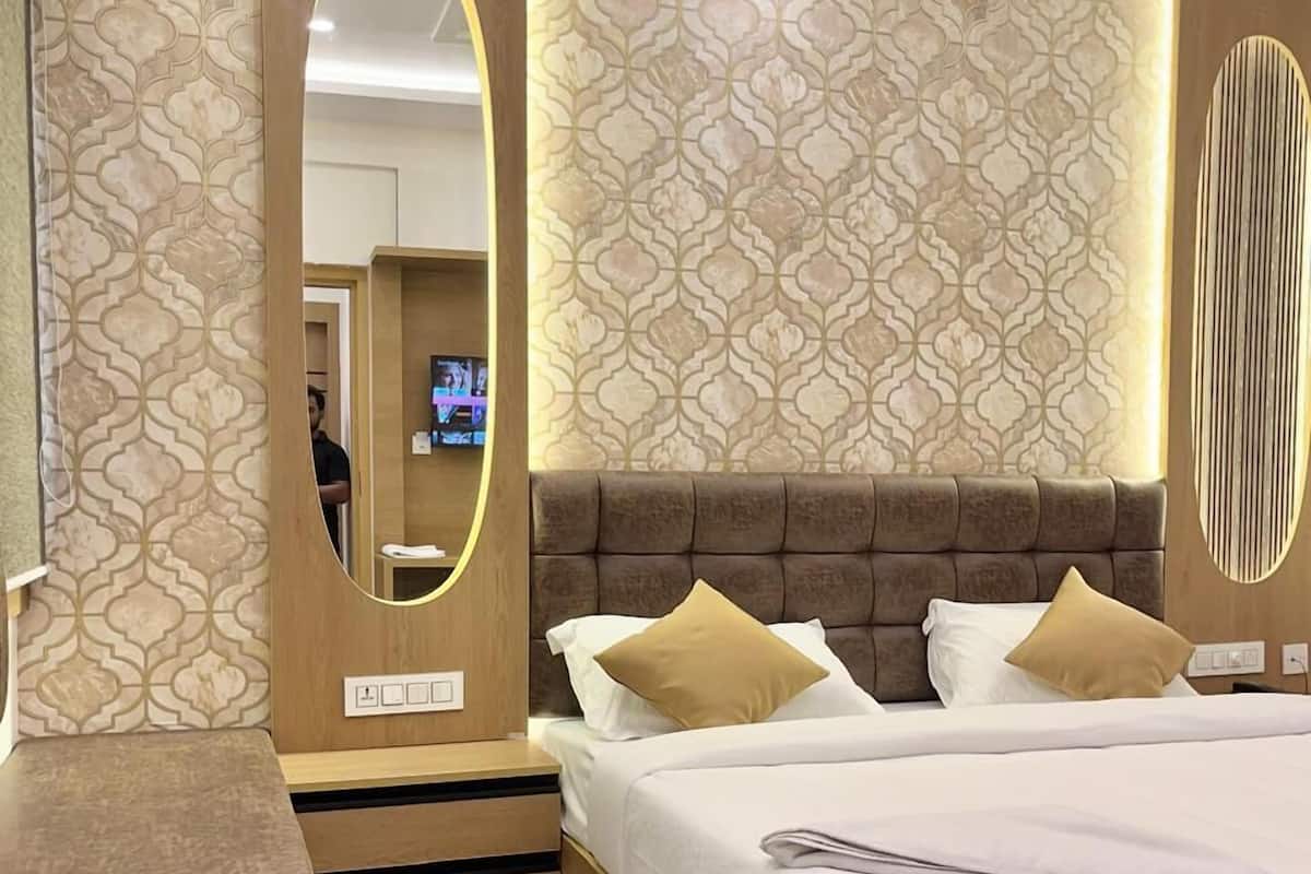 A modern hotel room with a large bed, a wooden nightstand, a mirror, and patterned wallpaper.