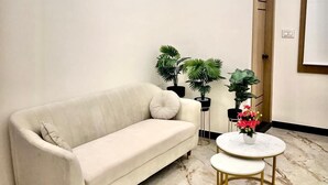 A modern living room with a beige sofa, two small side tables, and a marble floor. - Uptown Inn (Bengaluru)