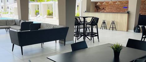 Ein moderner Essbereich im Freien mit schwarzem Mobiliar, eine Lounge-Ecke am Pool und Blick auf eine Stadtlandschaft.