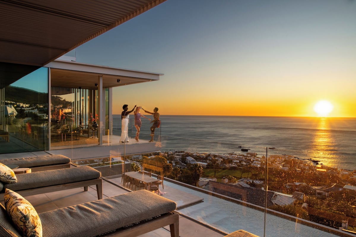 A modern outdoor lounge area with a glass balustrade overlooking a coastal view during sunset.