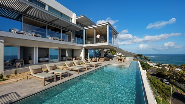 Een modern hotel met een zwembad, ligbedden en uitzicht op zee.