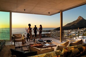 A spacious living area with a large glass wall offering a view of a mountain and a coastal town. - An African Story by RETURN Africa (Cape Town)
