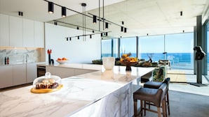 Een moderne keuken met een marmeren aanrechtblad, hanglampen en uitzicht op de oceaan.