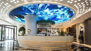 Een lobby met een groot digitaal plafondscherm, een receptiebalie en een modern interieur.