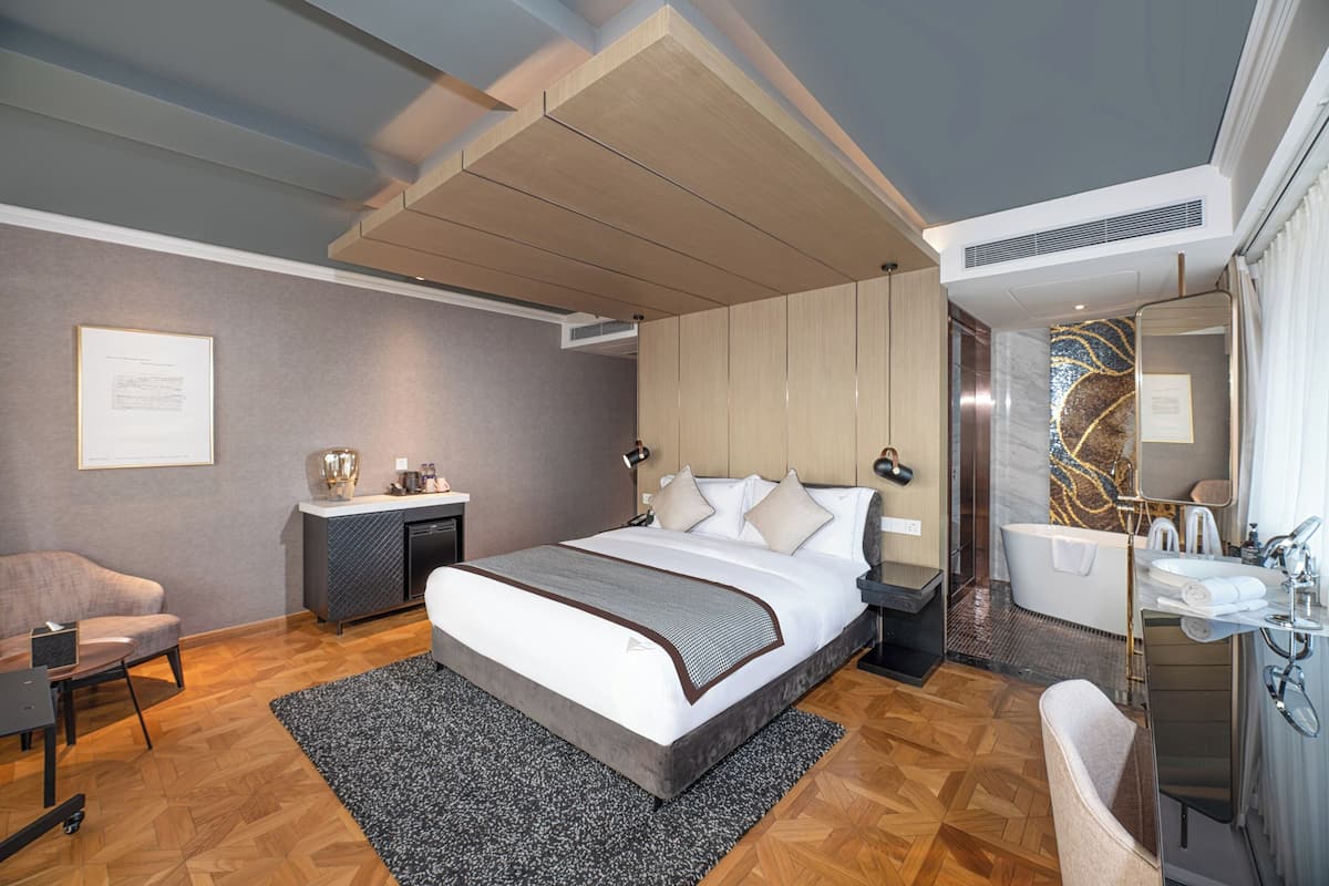 Una habitación de hotel moderna con una cama grande, un área de descanso, un baño con bañera y un escritorio.