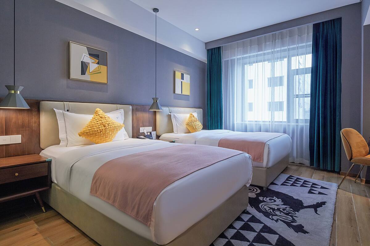Habitación de hotel con dos camas, una mesita de noche, una silla y un ventanal con cortinas.