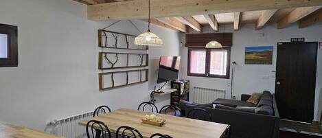 A cozy living space with a wooden ceiling, a dining table with chairs, a sofa, and a television.