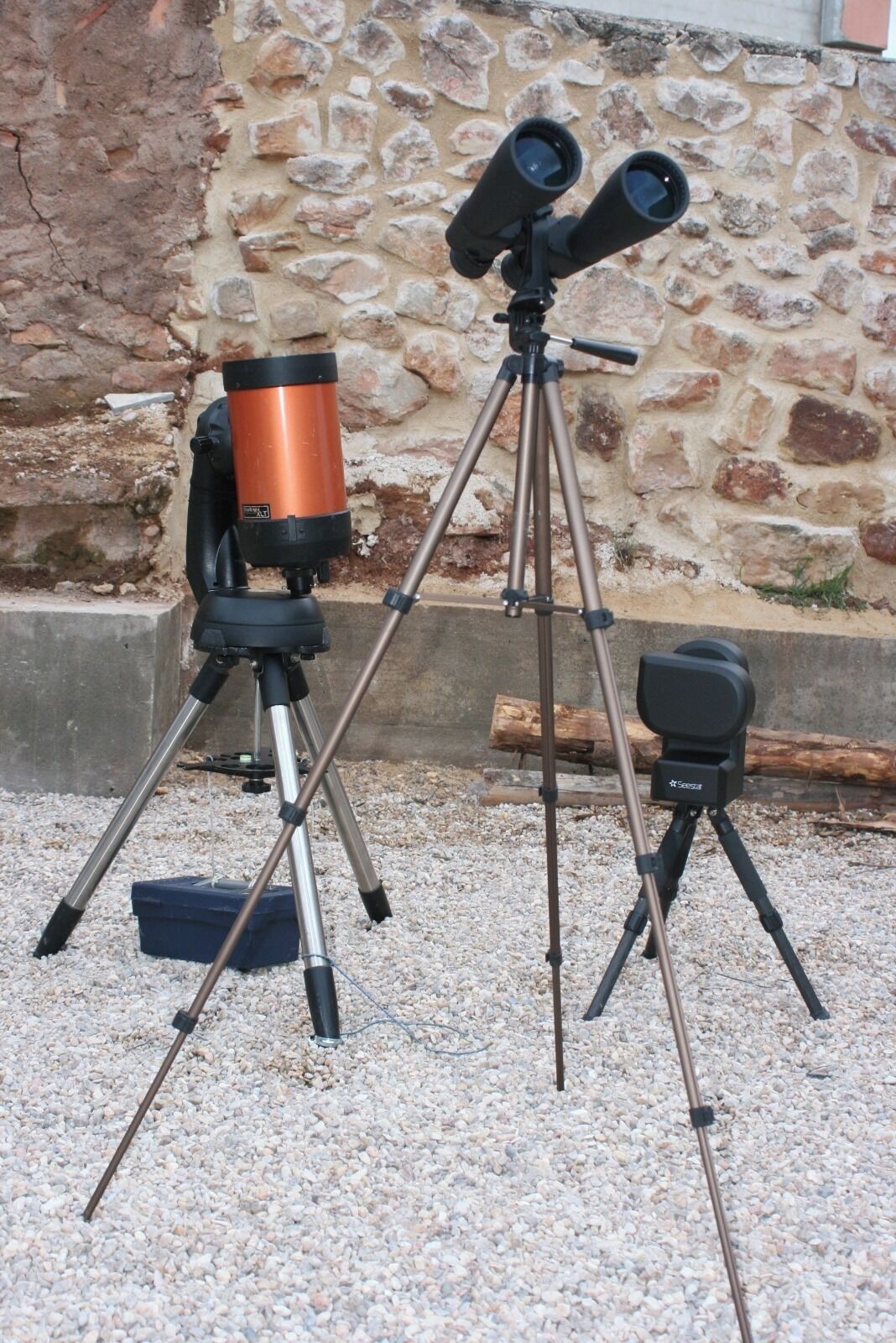 A telescope on a tripod with a stone wall in the background.