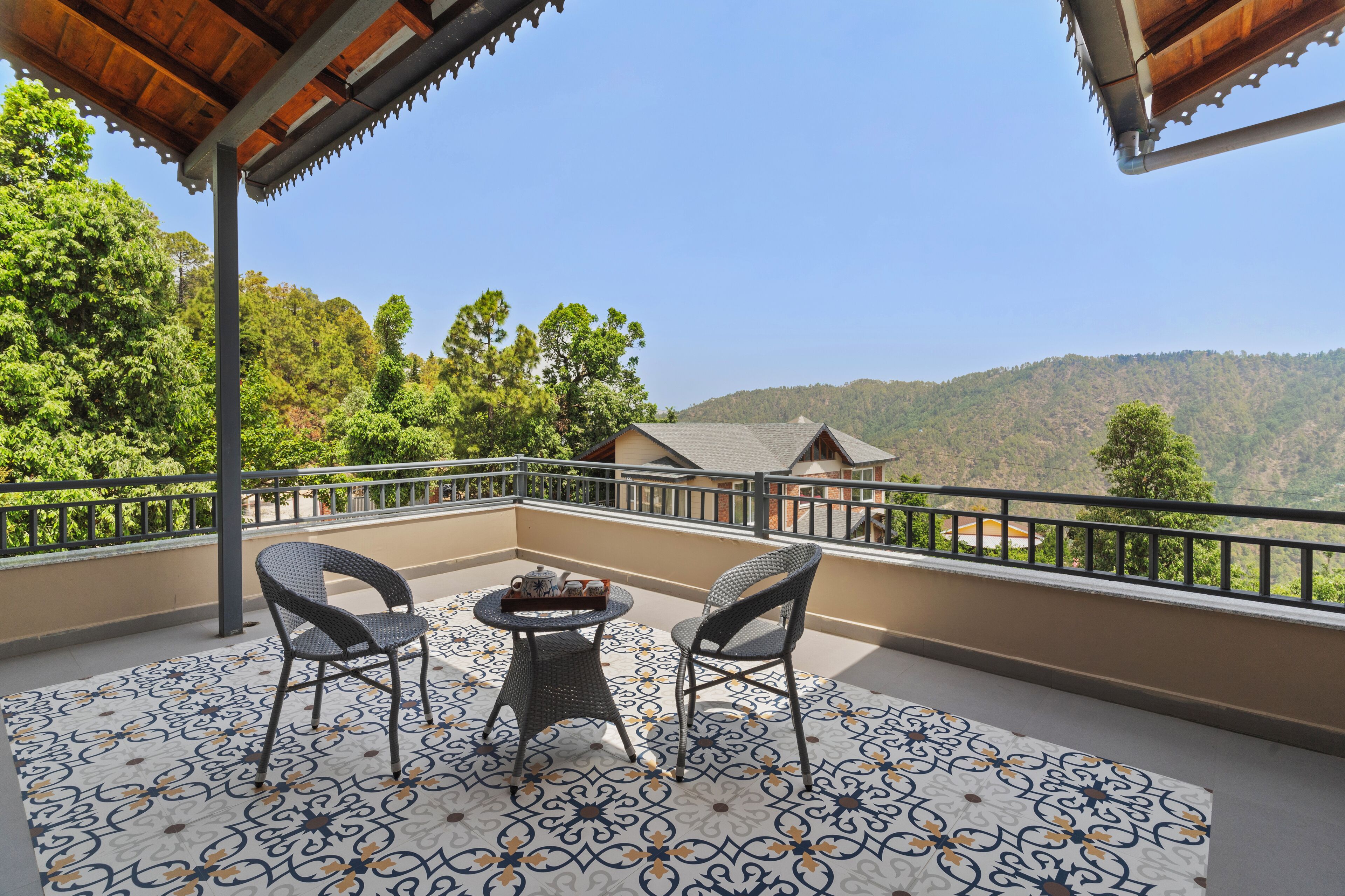 A balcony with two wicker chairs and a small table, overlooking a mountainous landscape.