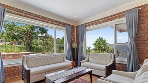 A room with two sofas facing a large window, a wooden coffee table, and a patterned rug. - Himvan by Akama Homes (Dhari)