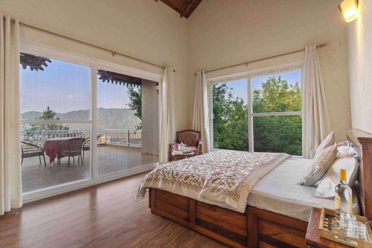 A bedroom with a large bed, a nightstand, a table with a chair, and a balcony with a table and chairs.
