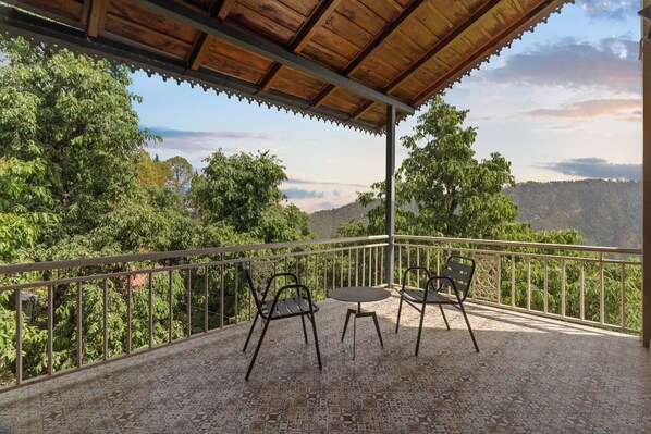 A covered terrace with two chairs and a table, overlooking a mountainous landscape. - Himvan by Akama Homes (Dhari)