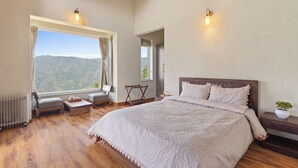 A bedroom with a large bed, a view of the outdoors, and a window with curtains. - Himvan by Akama Homes (Dhari)
