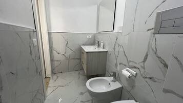 Casa de banho com sanita, bidé e lavatório, tudo com pavimento e paredes em mármore.