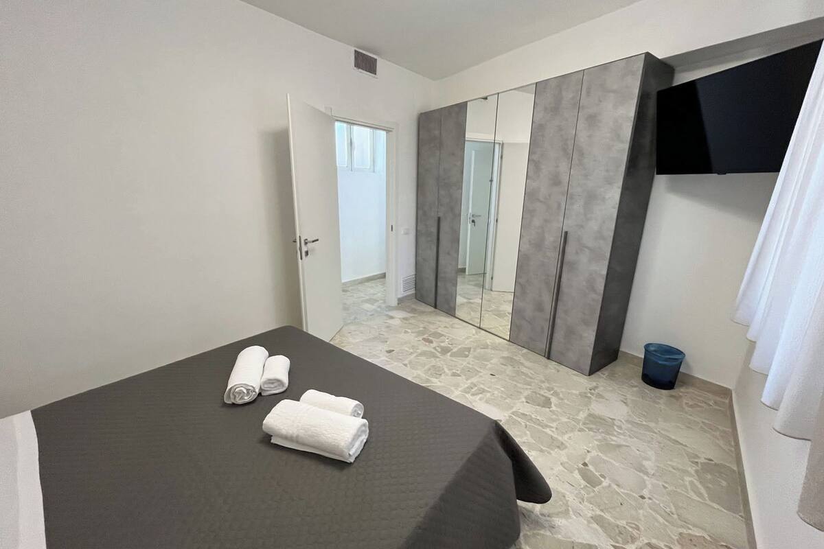 Ein Schlafzimmer mit einem Bett, zwei Handtüchern, einer blauen Mülleimer und einem Kleiderschrank mit Spiegel.