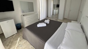 A hotel room with a bed, a dresser, a mirror, a television, and a wardrobe. - Suite Costa Sicana (Siculiana)