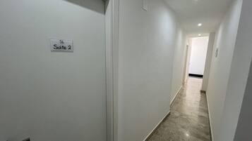 A hallway with a sign reading "Suite 2" on a white door. The walls are plain and the floor is tiled.