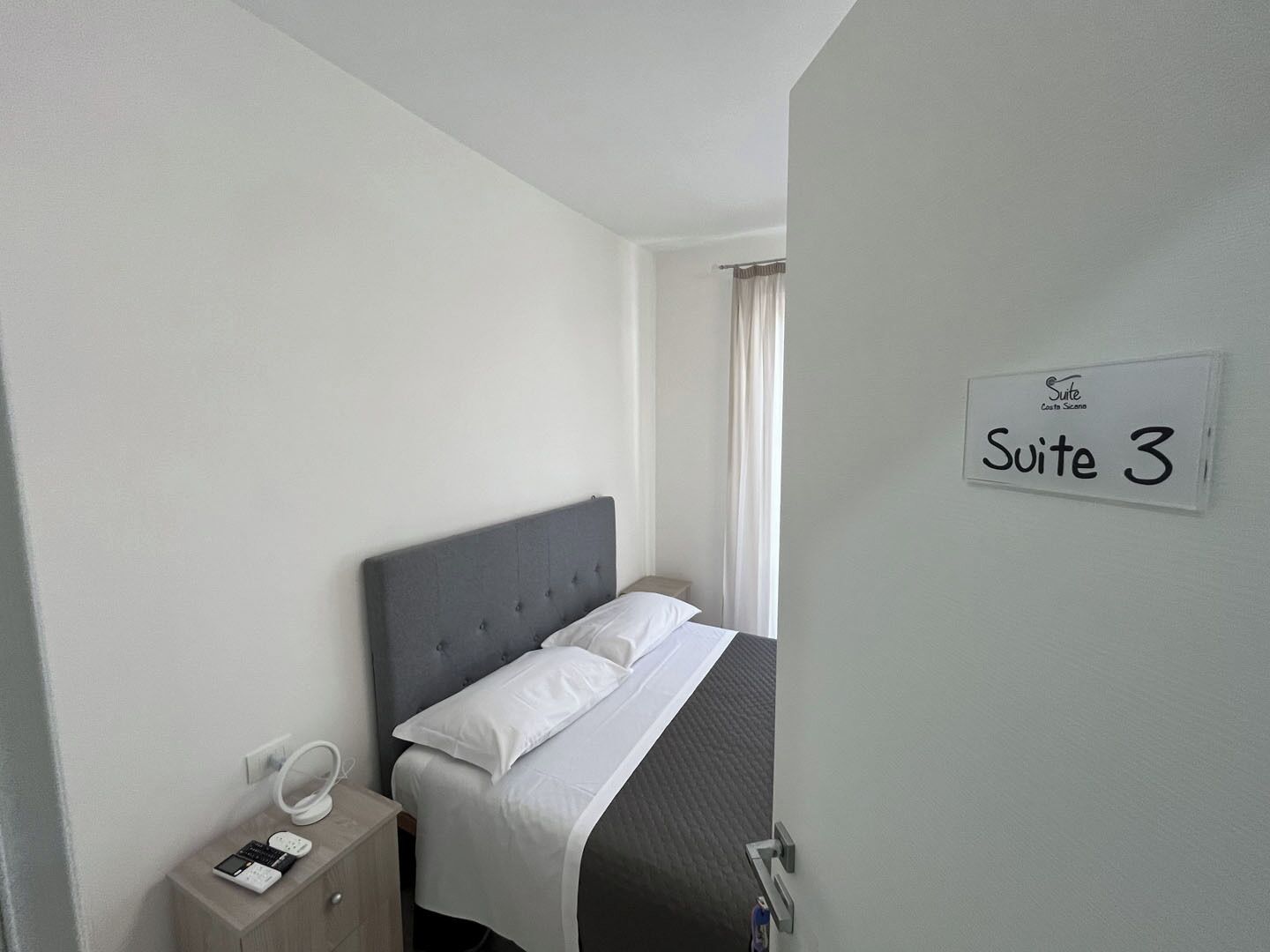 Ein Hotelzimmer mit einem Bett, einem Nachttisch mit Lampe und einem Schild, auf dem 'Suite 3' steht.