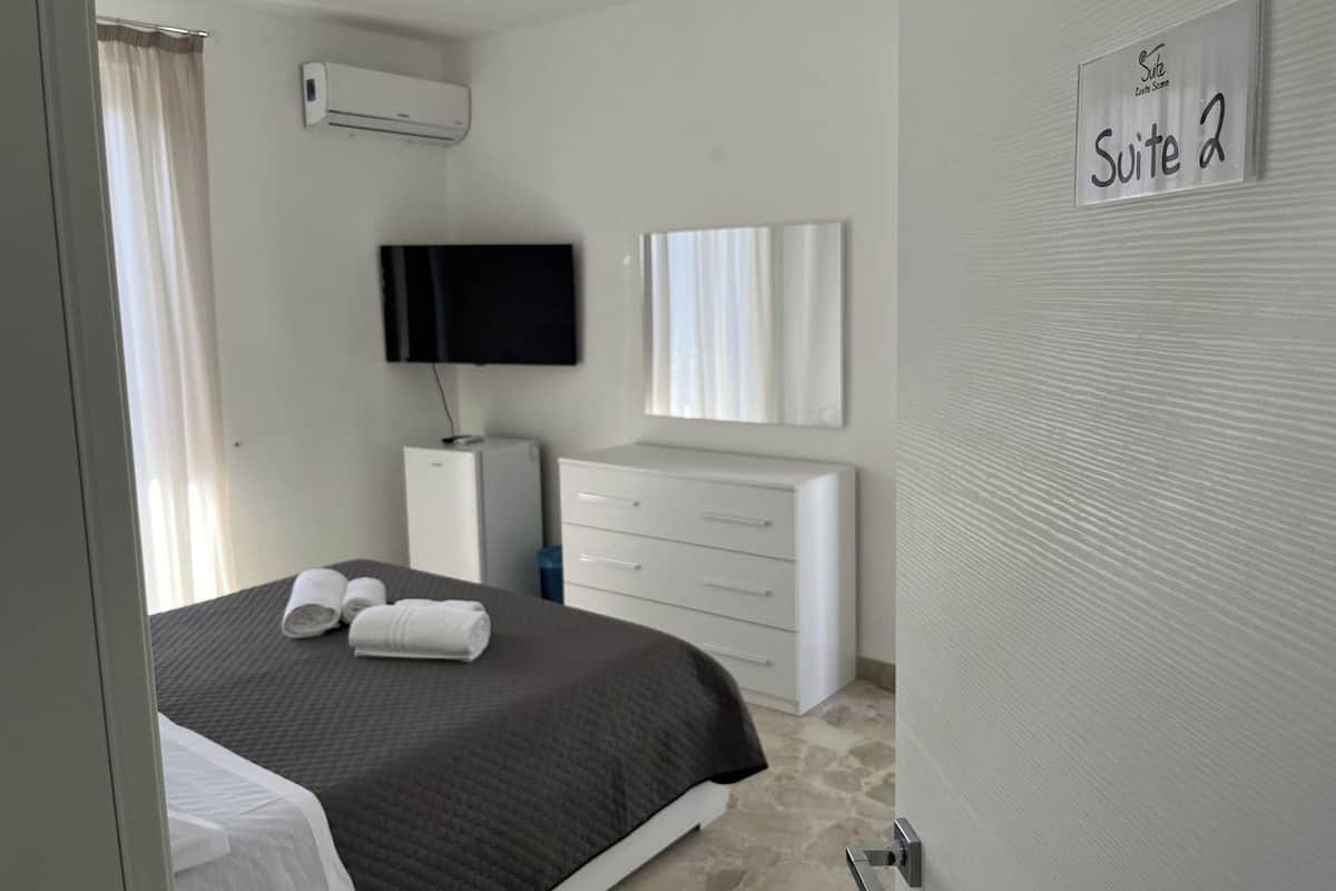 Ein Hotelzimmer mit Bett, Fernseher, Kommode und einem Schild mit der Aufschrift 'Suite 2'.