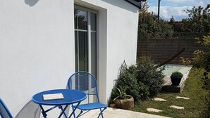 Eine Terrasse mit Tisch und Stühlen, einer weißen Wand und einem Holzzaun im Hintergrund.