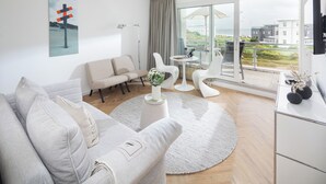 Un salon moderne avec un canapé, des fauteuils, une table basse et une vue sur la ville grâce à de grandes fenêtres.
