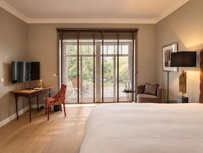A hotel room with a large bed, a desk with a flat-screen TV, a chair, and a view through a window with blinds. - THE RESET (Groß Plasten)
