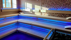 Ein moderner Wellnessraum mit Holzlamellenbänken, einer Wand aus gestapelten Baumstämmen und einem Fenster mit Tageslicht.