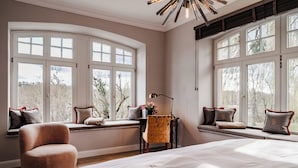Een slaapkamer met een groot bed, een raamzitplaats met een stoel en een bureau met een lamp.