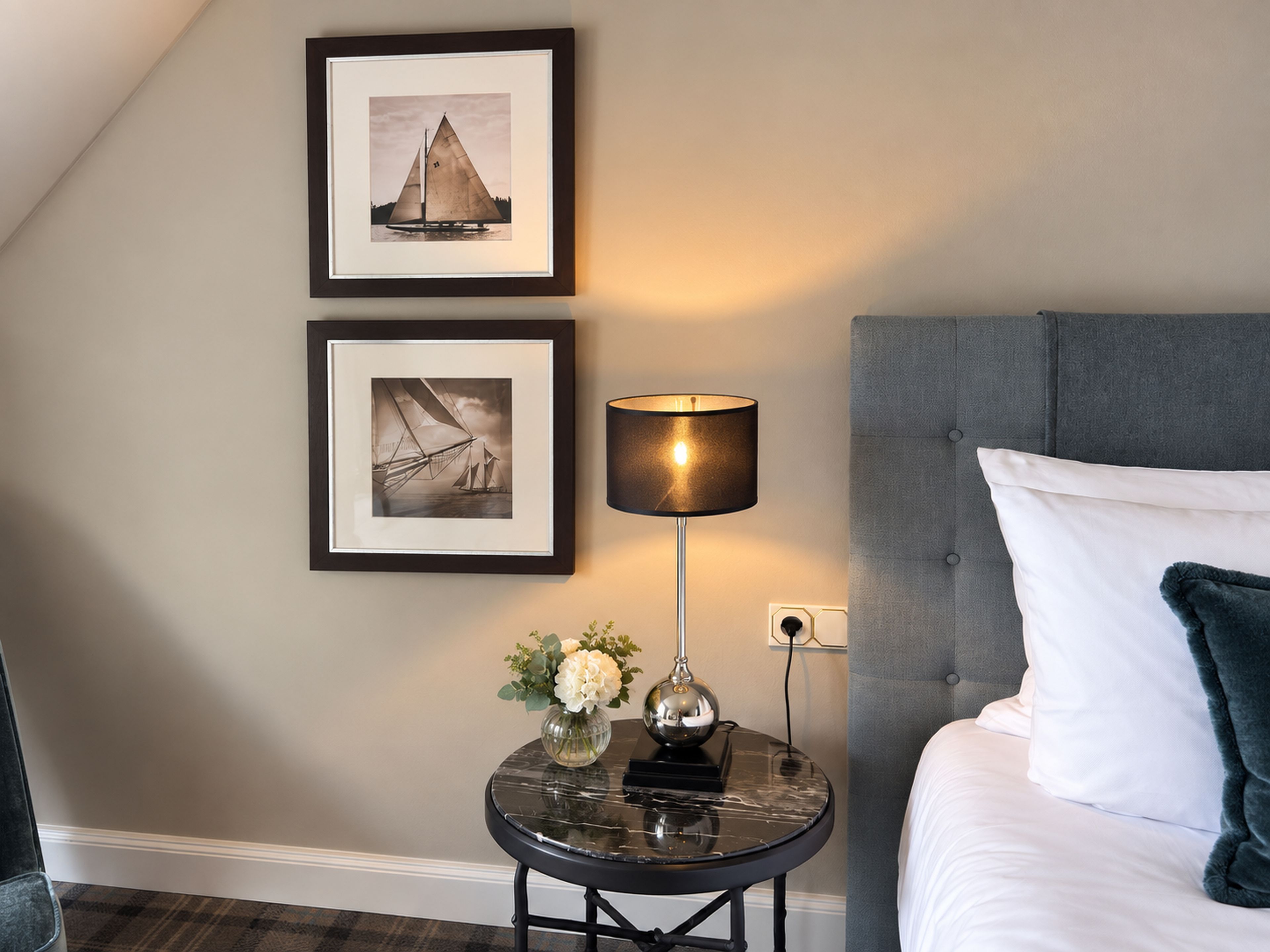Une chambre à coucher avec un lit, une table de chevet avec une lampe et deux tableaux encadrés accrochés au mur.