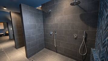 A modern bathroom with dark tiles, a shower area, and a visible vent.