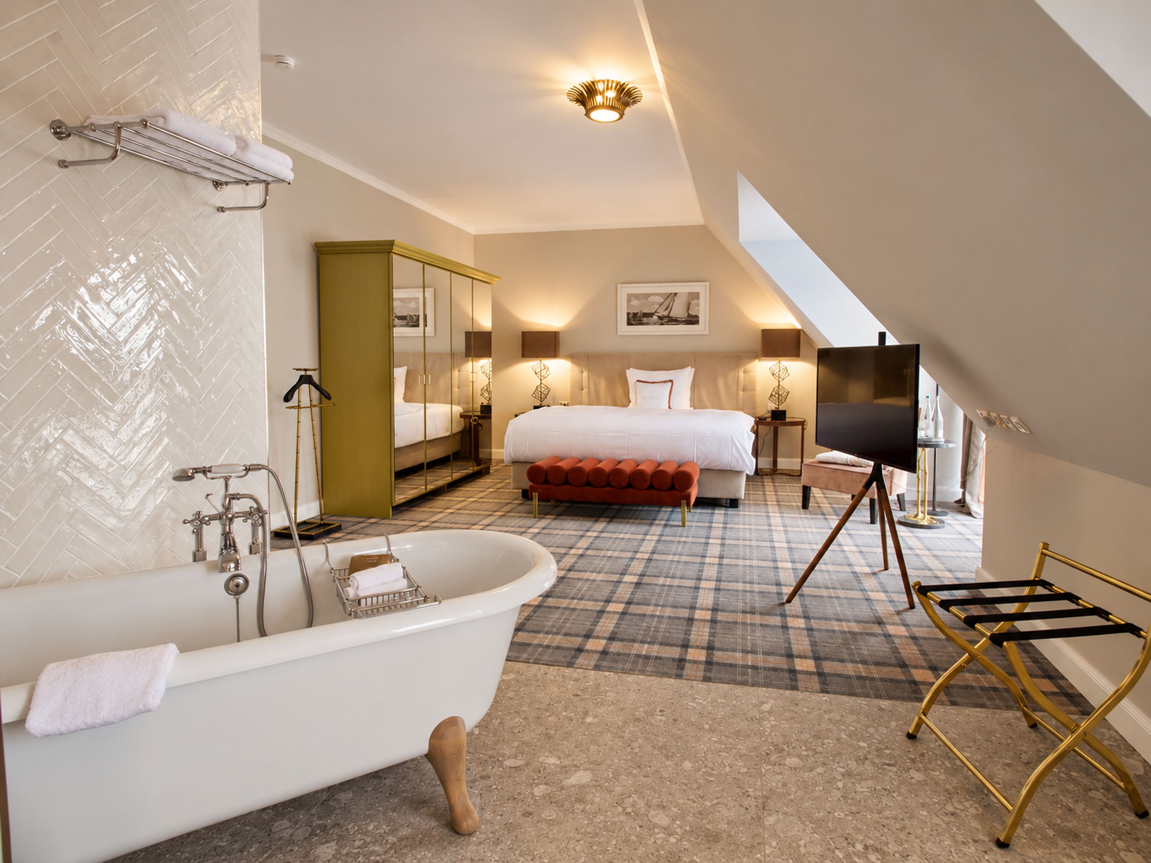 Ein modernes Hotelzimmer mit einer großen Badewanne, einem Bett mit rotem Kopfteil, einem Gemälde an der Wand und einem Fernseher auf einem Schrank.