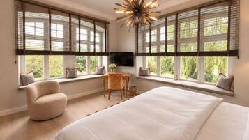 A bedroom with a large bed, a desk with a chair, a television, and windows with blinds.