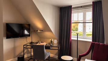 A hotel room with a desk, chair, TV, and a view of a building through the window.