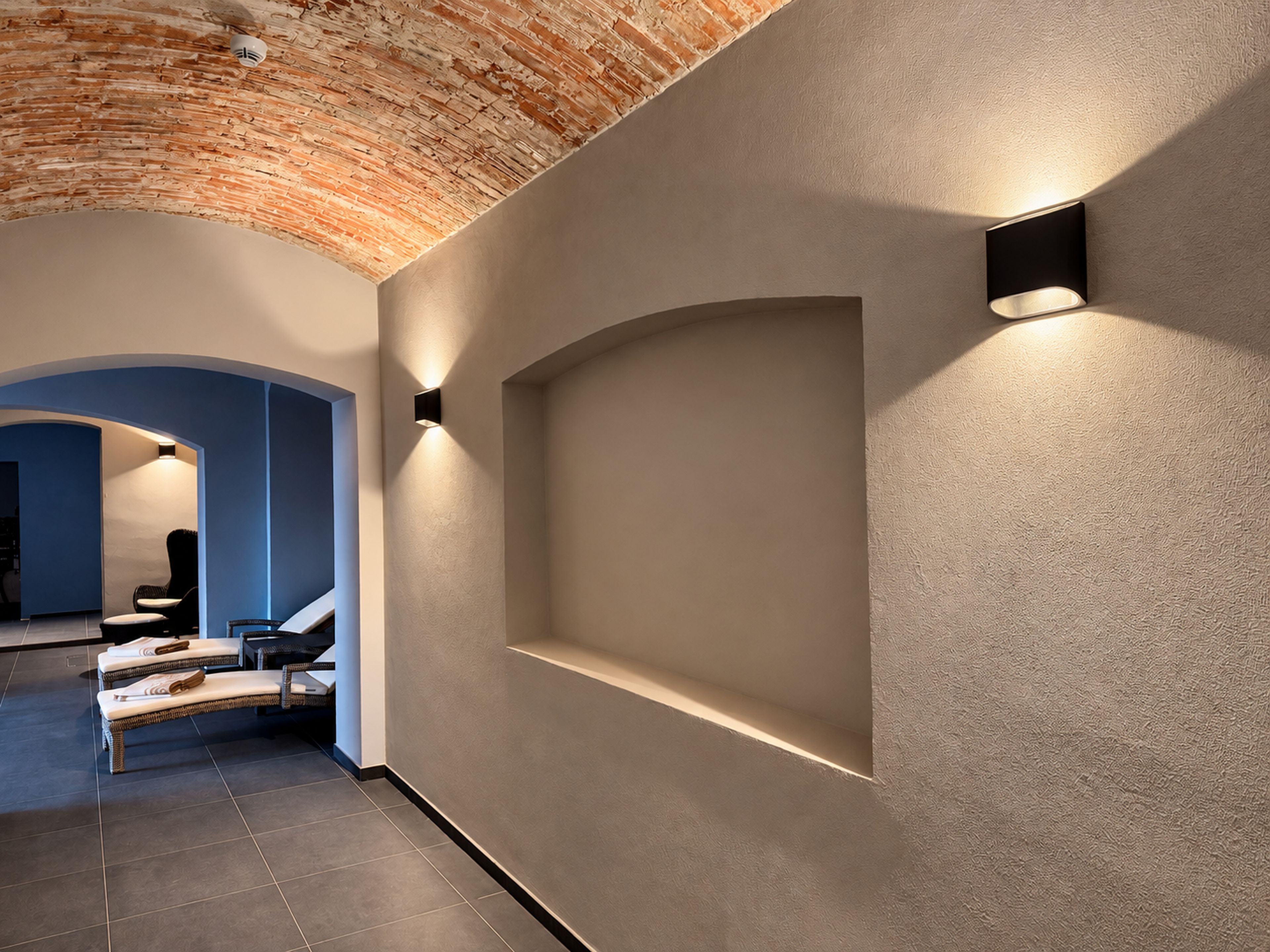 A hallway with a brick ceiling, recessed lighting, and a seating area with chairs and a sofa.