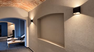 A hallway with a brick ceiling, recessed lighting, and a seating area with chairs and a sofa.