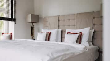 A neatly made bed with white linens and red-trimmed pillows, a beige upholstered headboard, and a bedside lamp.