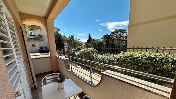 Un balcon avec une table et une chaise, un pot de fleurs et une vue sur la rue et la verdure.