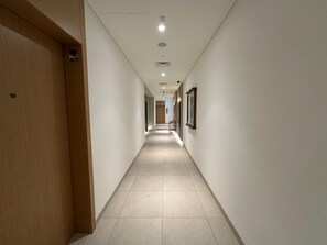 A hallway with a wooden door on the left, a tiled floor, and framed pictures on the right wall.