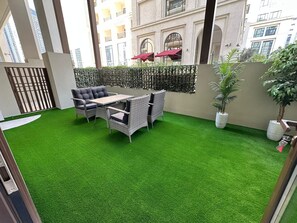 An outdoor patio with artificial grass, wicker furniture, and potted plants.