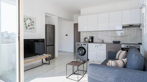 A modern apartment with a living room, a kitchen with a washing machine, and a large window. - Rosemont Studio With Balcony in Larnaca (Larnaca)