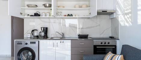 A modern kitchen with built-in appliances, a washing machine, and a grey sofa with a striped pillow.