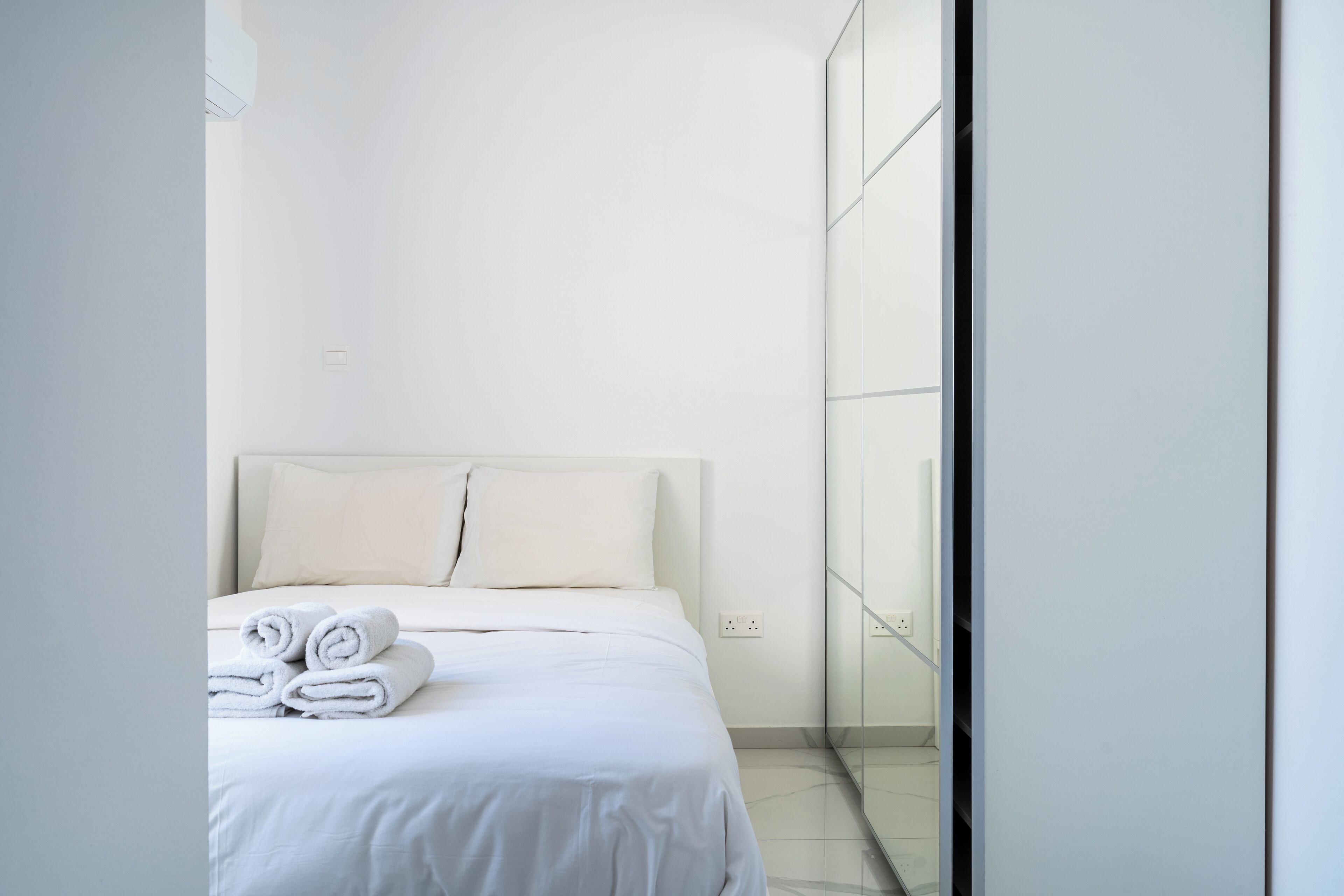 Una camera d'albergo moderna con un letto rifatto, un grande specchio e un design minimalista.