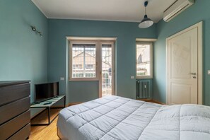 A bedroom with a bed, a desk, a TV, and a window.