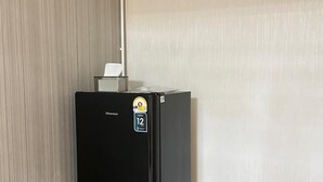 A compact black refrigerator in a corner of a room with light wooden flooring and a plain white wall. - Far Far Away Hostel Chiangmai (Chiang Mai)